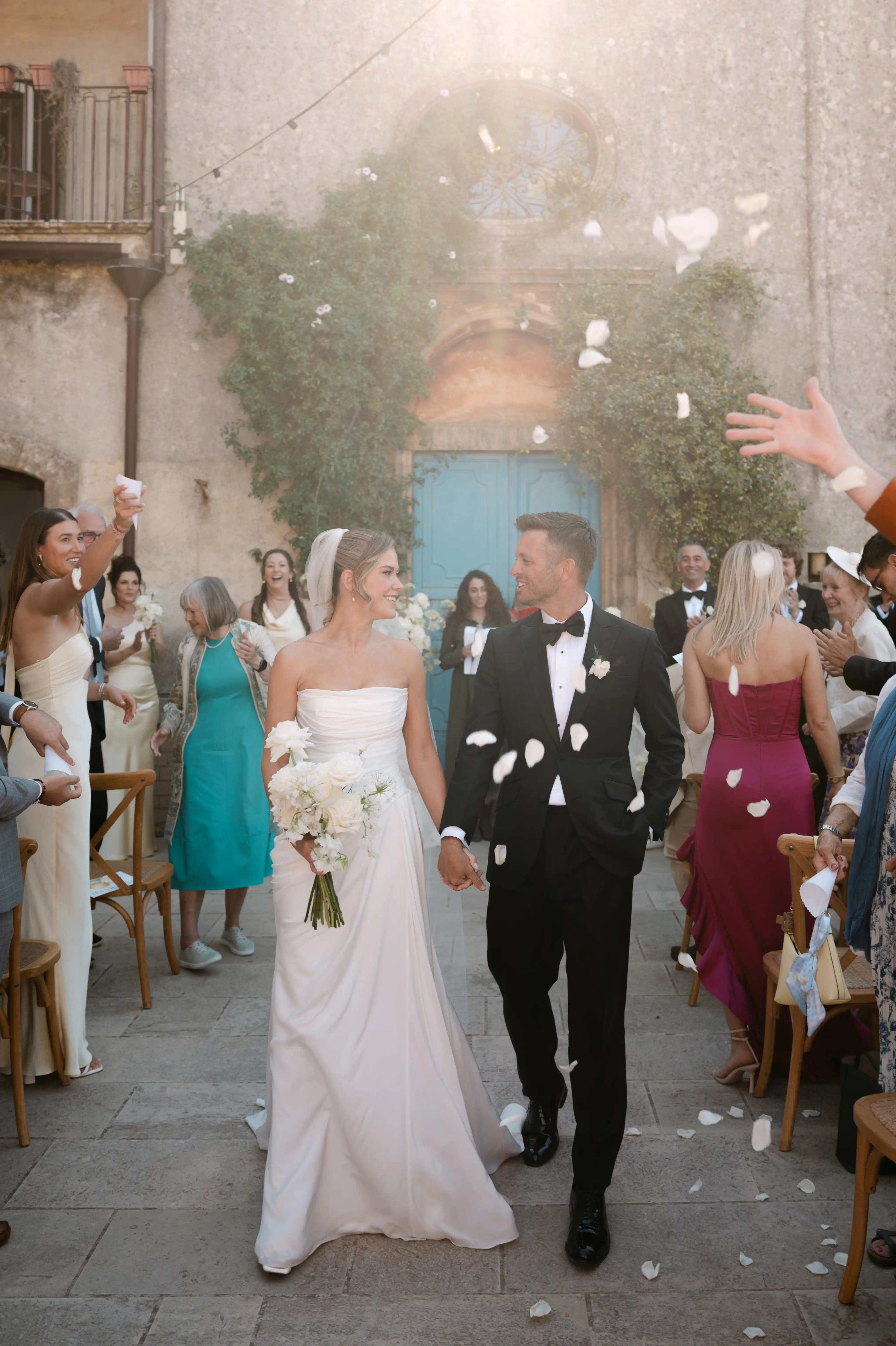Newlywed couple walking through flower petals after their outdoor wedding ceremony in Sicily.